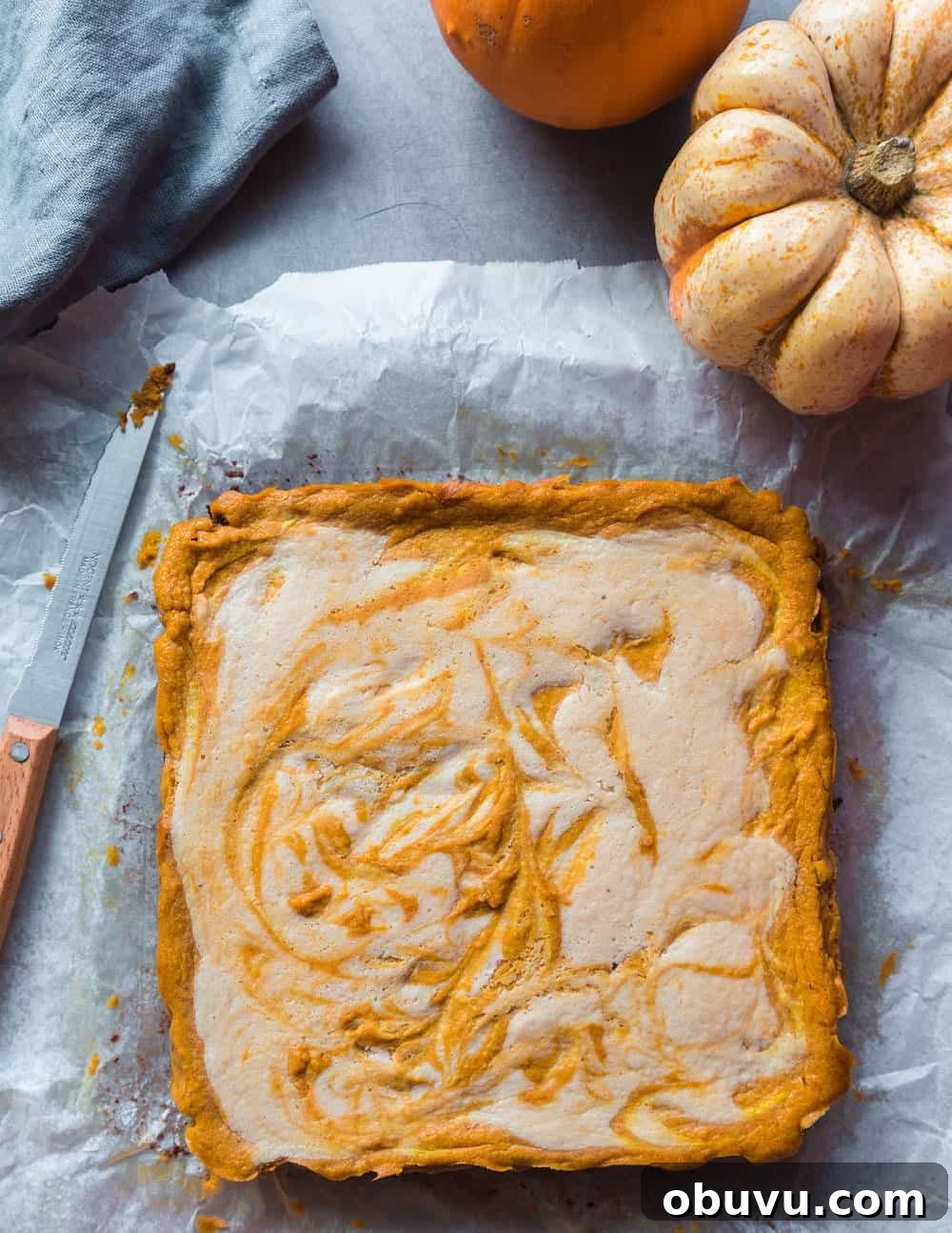 Vegan Baked Pumpkin Cheesecake Bars — Creamy Fall Dessert 2 Full square unsliced pumpkin cheesecake on parchment paper.
