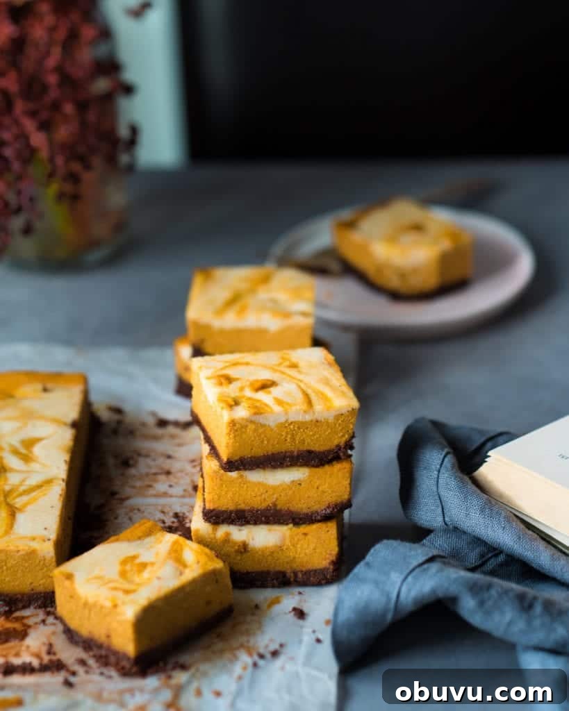 Vegan Baked Pumpkin Cheesecake Bars — Creamy Fall Dessert 4 Three cheesecake bars stacked in a pile. Next to other cheesecake bars.