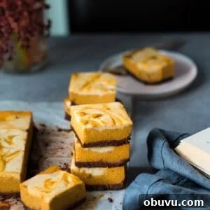 Vegan Baked Pumpkin Cheesecake Bars — Creamy Fall Dessert 8 Three cheesecake bars stacked in a pile. Next to other cheesecake bars.