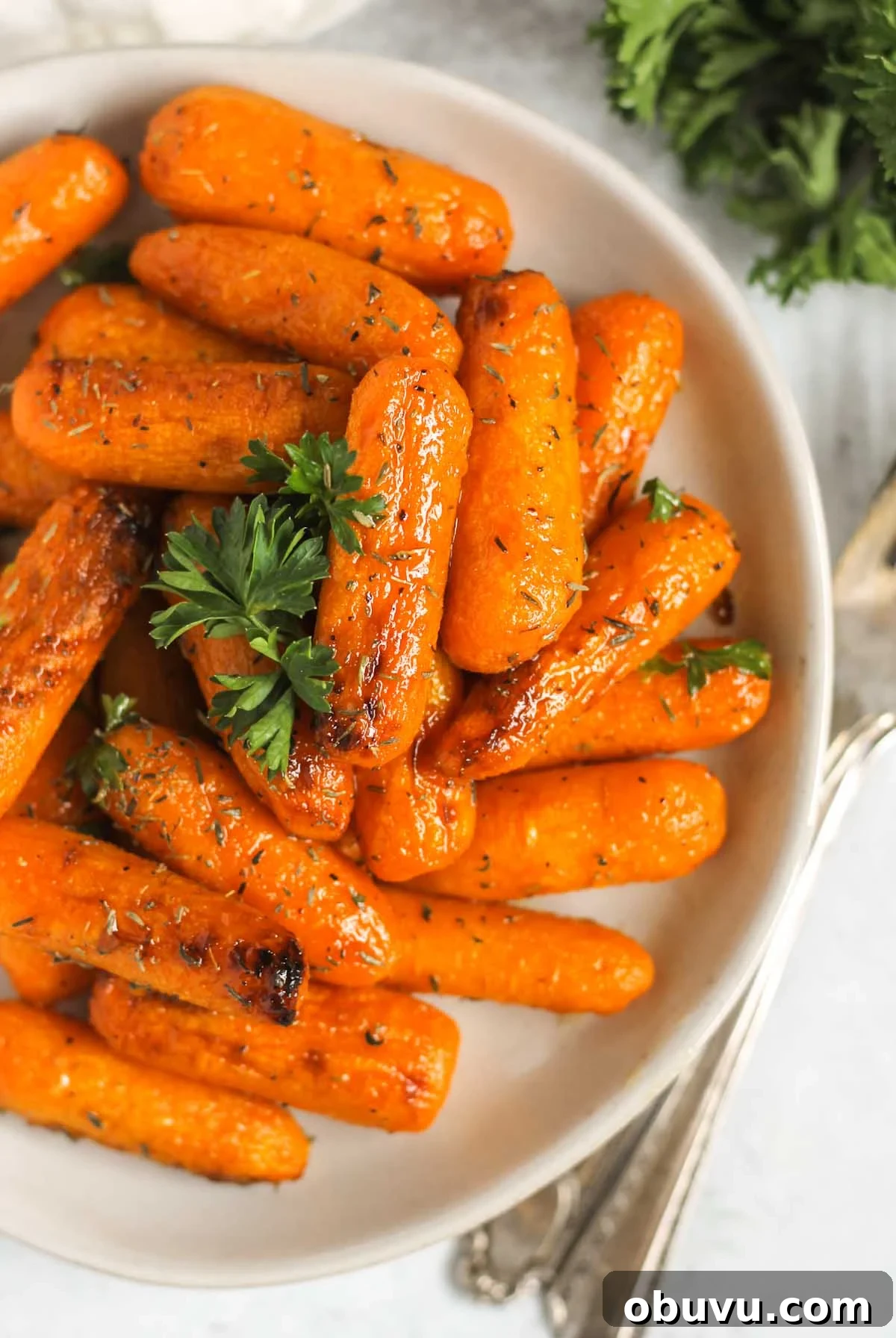 Roasted baby carrots sprinkled parsley on a small plate with vintage forks laying next to the plate.