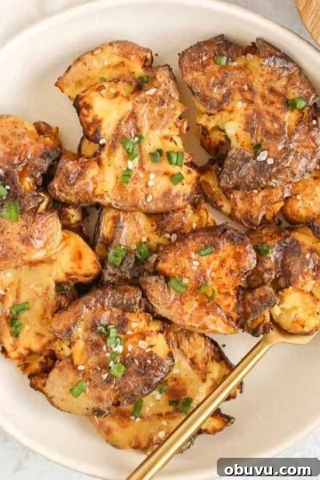 Fried smashed potatoes on a round serving plate with a gold fork.