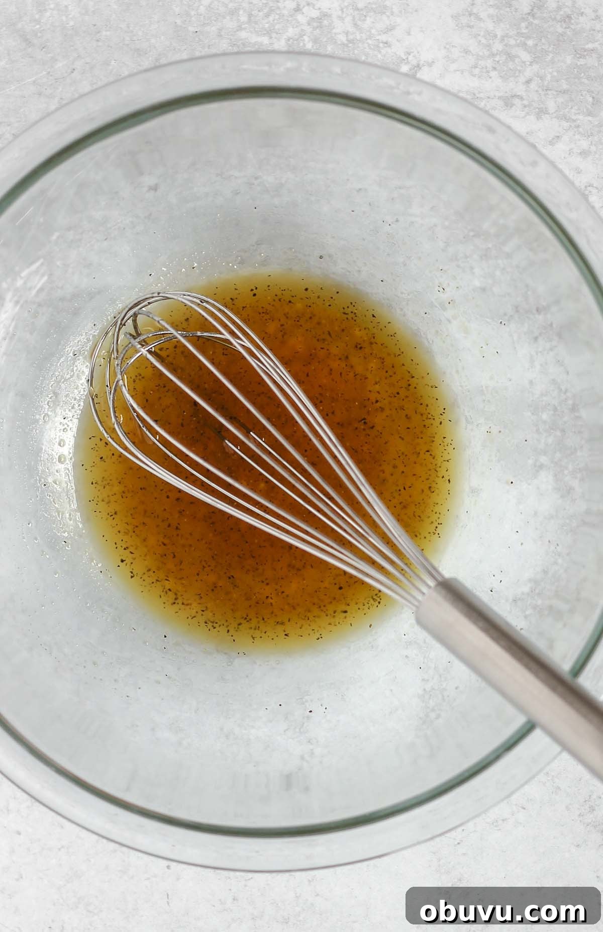 Wire whisk mixing honey marinade in a small glass mixing bowl.
