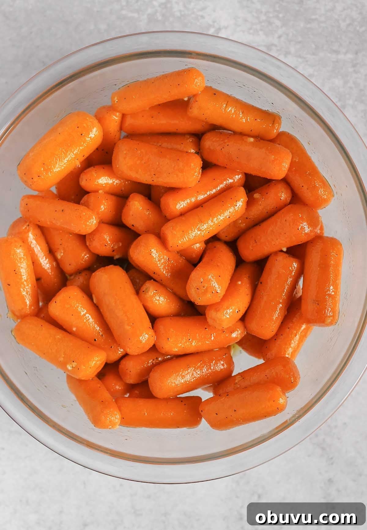 Baby carrots mixed with honey marinade in a glass mixing bowl.