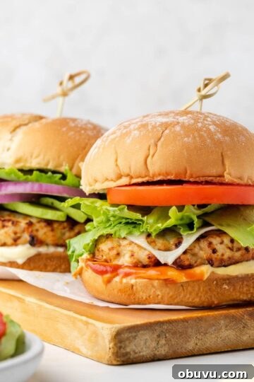 Two air fried turkey burgers with buns on a wood cutting board.