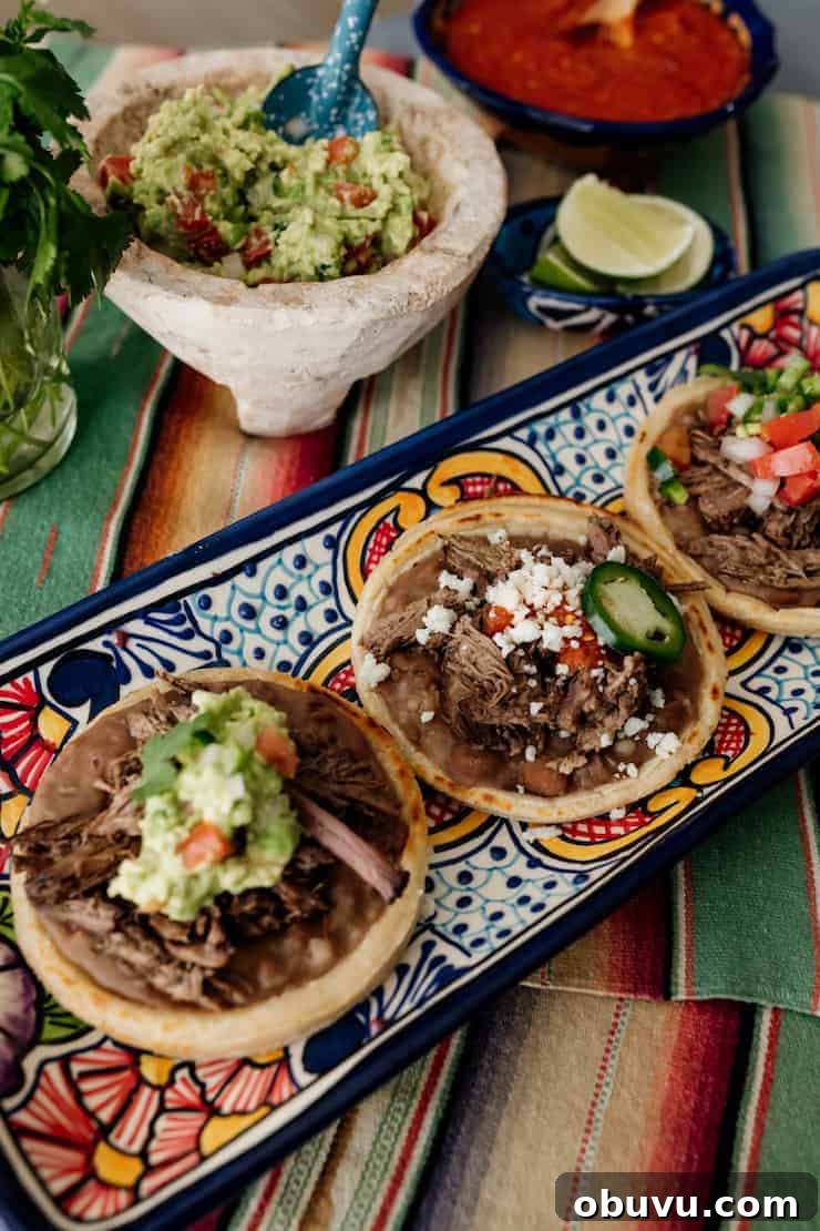 Brisket Sopes: Authentic Mexican Sopes de Carne Deshebrada 2 three beef brisket topped mexican sopes on a colorful rectangular serving platter with a bowl of guacamole and salsa in the background.