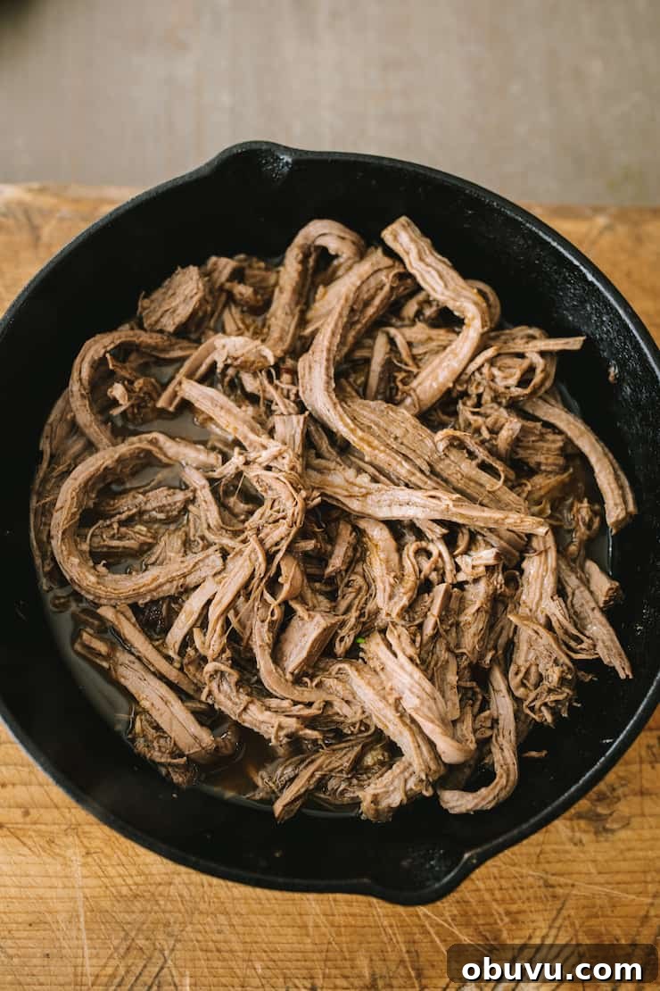 Brisket Sopes: Authentic Mexican Sopes de Carne Deshebrada 4 shredded slow cooker beef brisket and juices in a cast iron skillet on a wooden table.