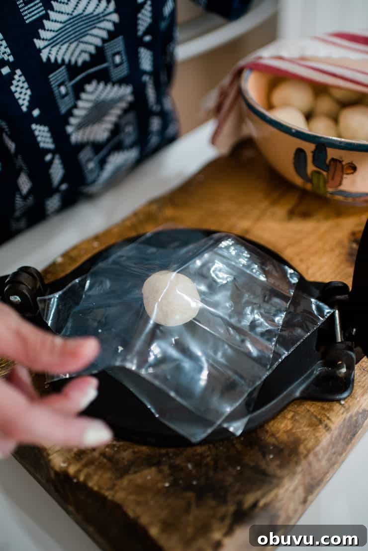 Brisket Sopes: Authentic Mexican Sopes de Carne Deshebrada 7 how to make Sopes step 2 - Tortilla Press on a big wooden board with a ball of sope dough between plastic sheeting.
