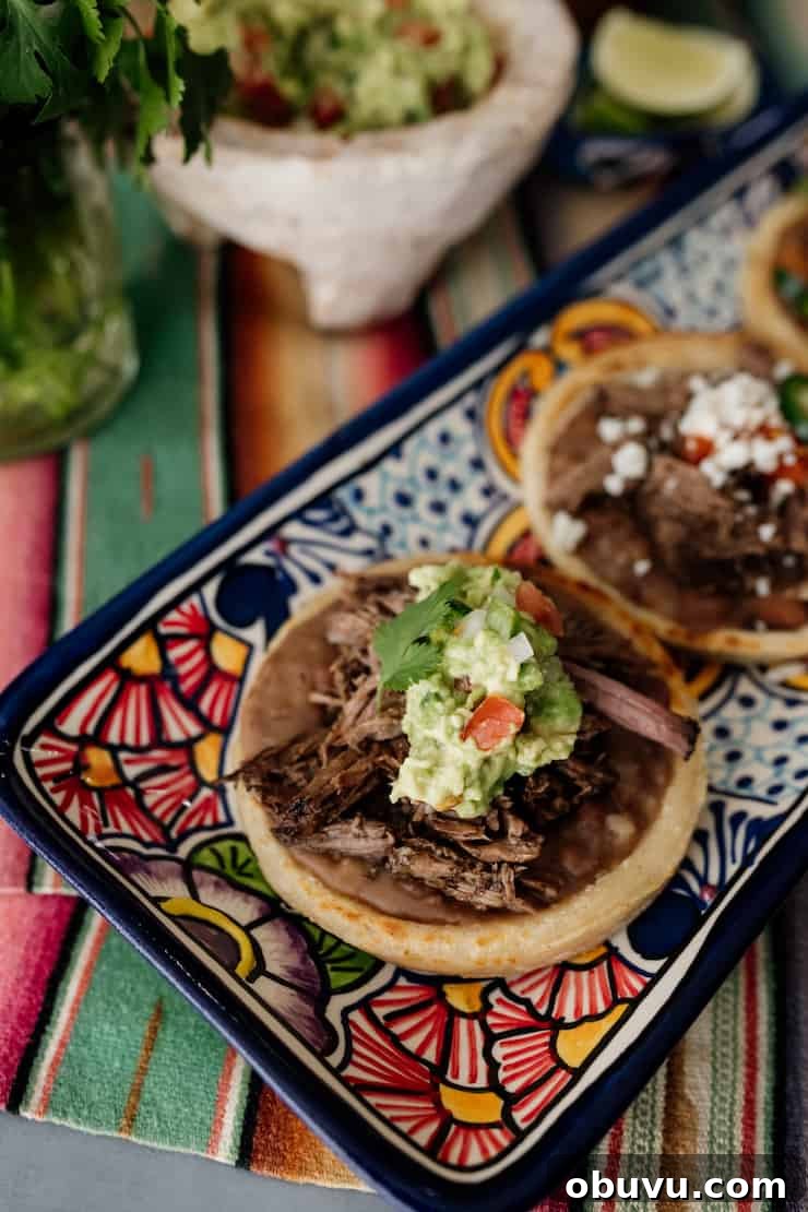 Brisket Sopes: Authentic Mexican Sopes de Carne Deshebrada 10 close up shot of colorfully painted rectangular serving dish with three sopes filled with refried beans, beef brisket and guacamole.