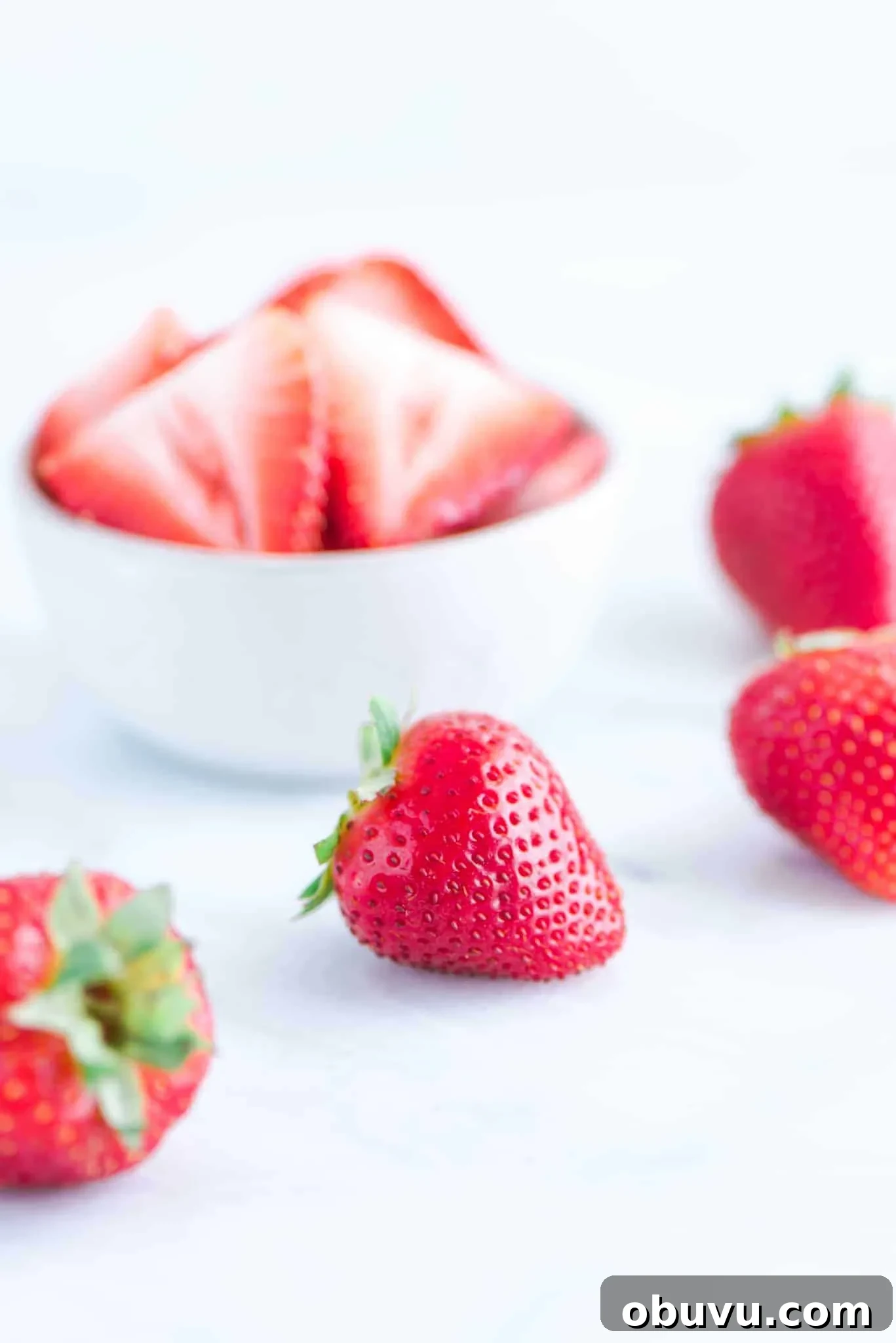 Gluten-Free Strawberry Icebox Cake Recipe for Summer Slices 3 sliced strawberries in a white bowl with whole strawberries on a marble slab