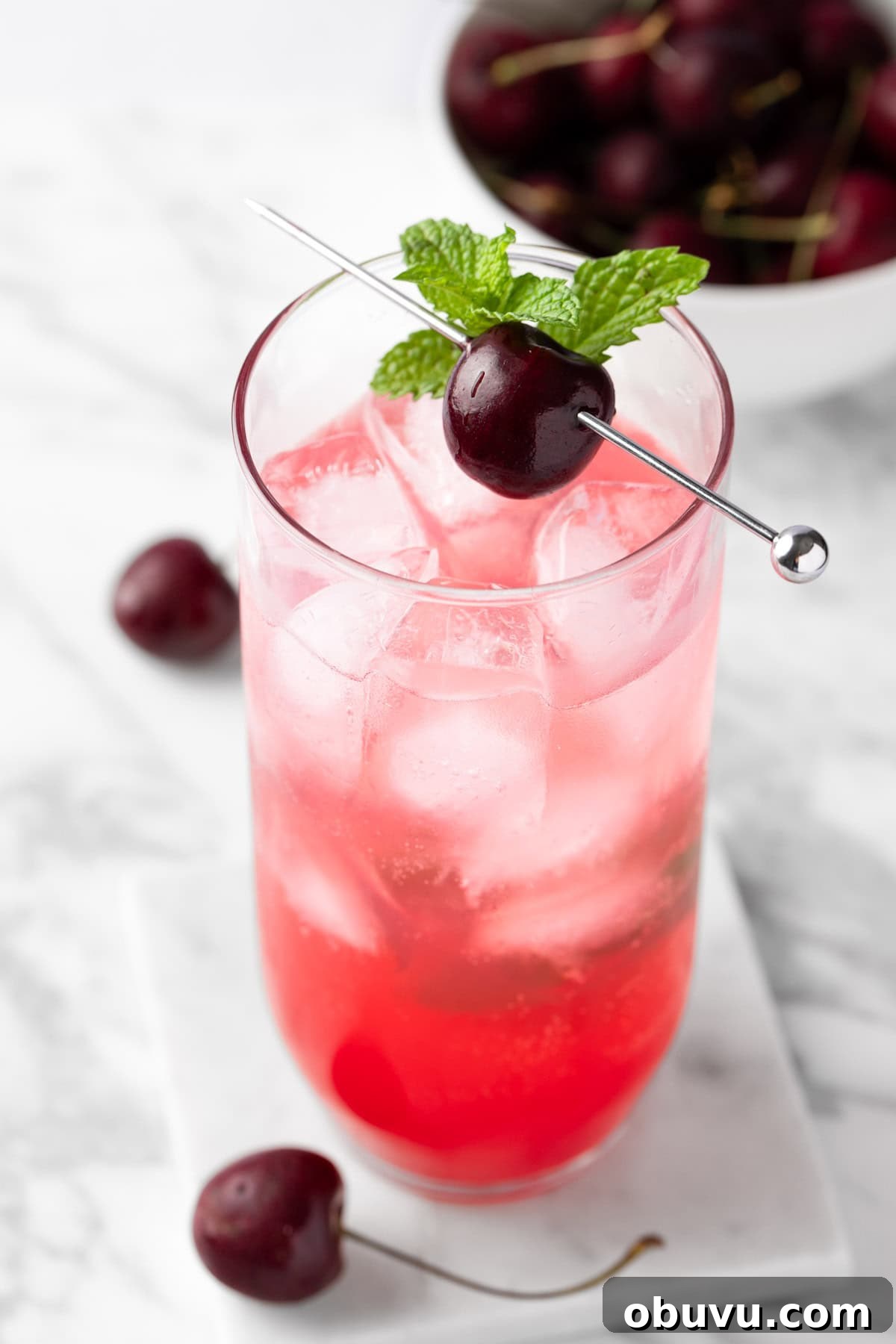 A black cherry mojito garnished with a fresh cherry and sprig of mint leaves.