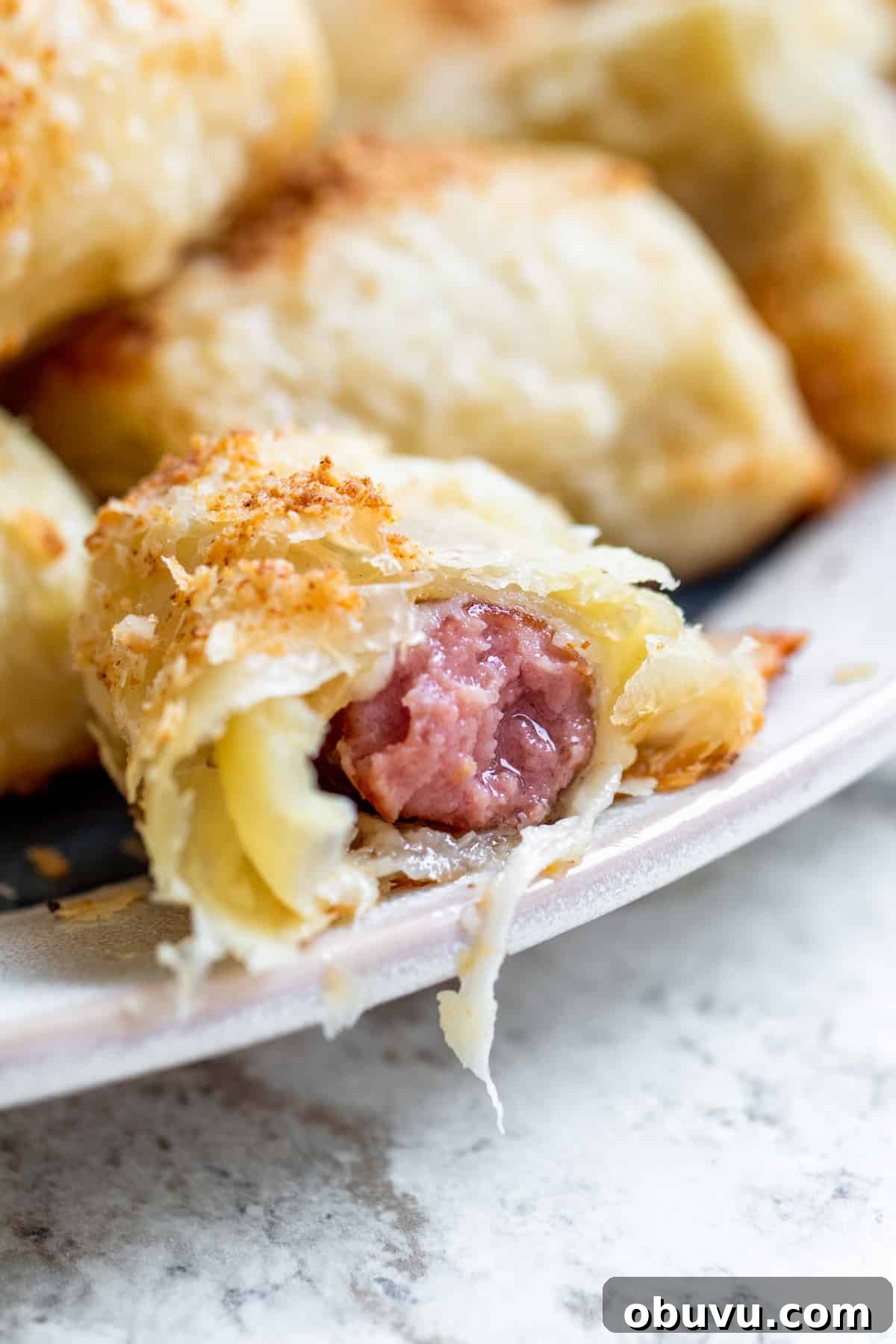 Cheesy Puff Pastry Pigs in a Blanket Recipe 6 Strait on shot of cheesy pigs in a blanket with bit out of it on plate.