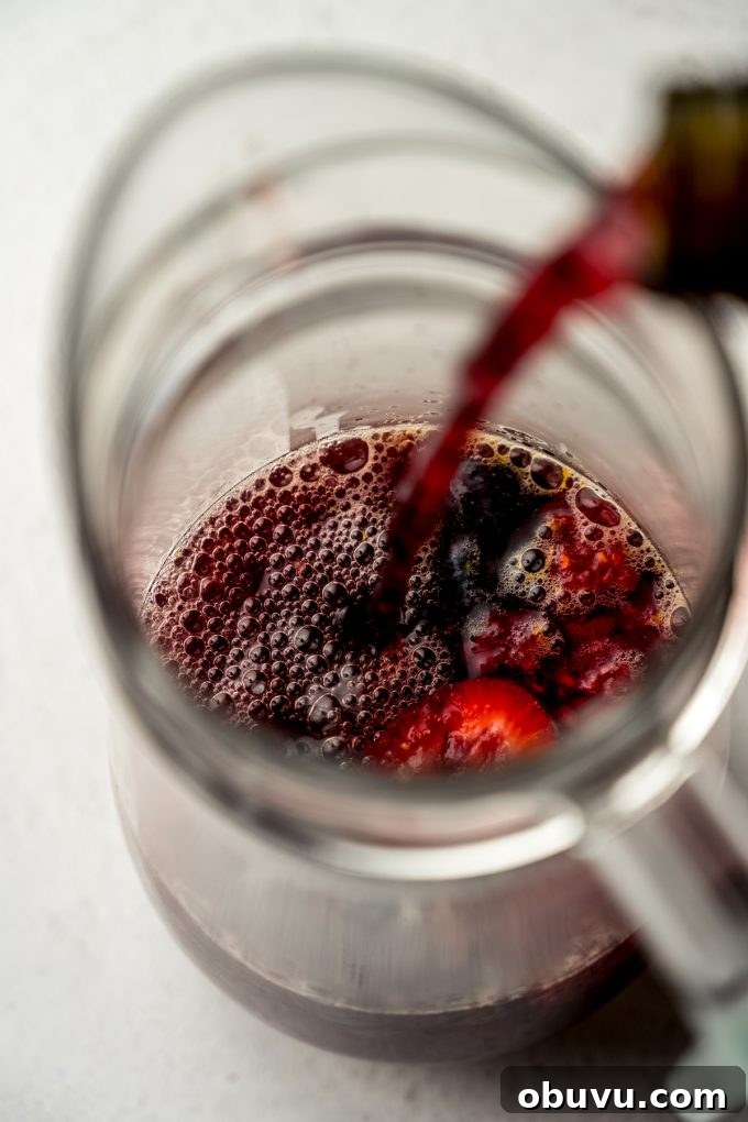 Berry Sangria and Berry Mocktail Recipes for Every Occasion 12 Aerial photo of someone pouring nonalcoholic wine into berry sangria in a pitcher.