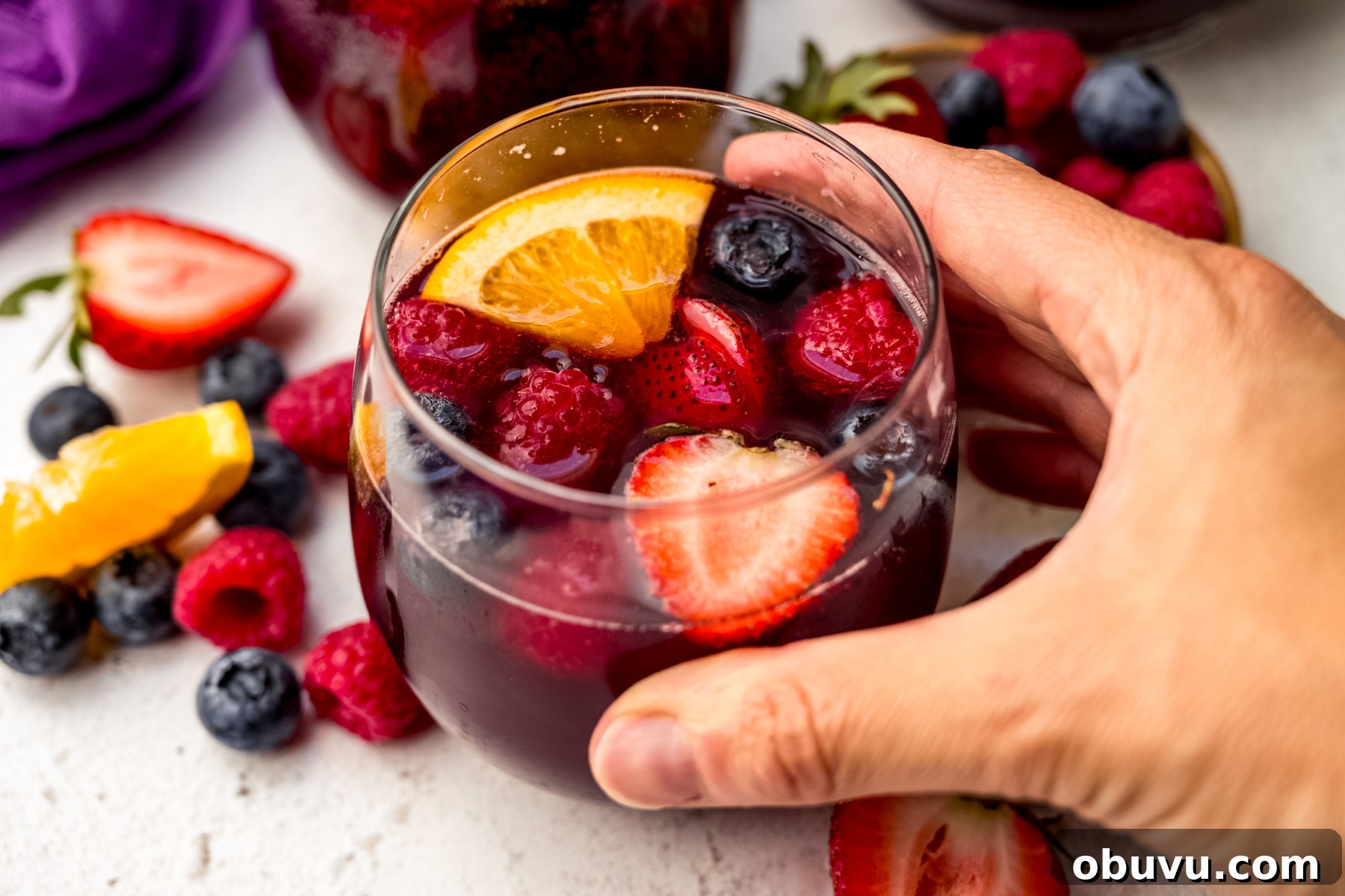 Berry Sangria and Berry Mocktail Recipes for Every Occasion 5 Someone's hand around a glass of berry sangria.