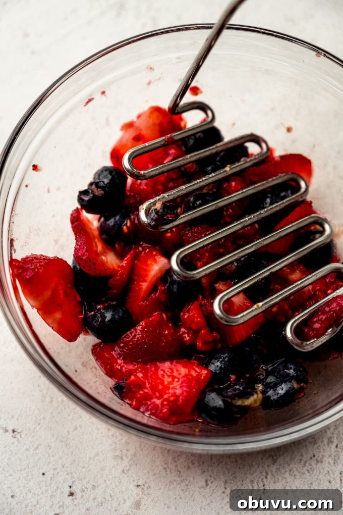 Berry Sangria and Berry Mocktail Recipes for Every Occasion 7 A bowl of blueberries, strawberries, and raspberries getting macerated with a potato masher.