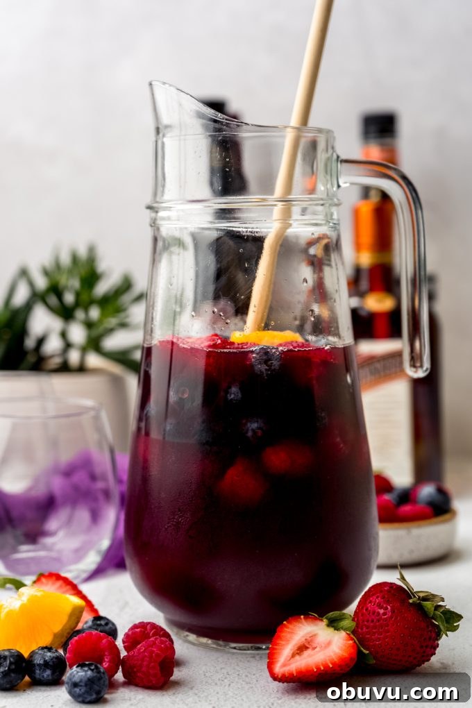 Berry Sangria and Berry Mocktail Recipes for Every Occasion 9 A glass pitcher of berry sangria with a wooden spoon in it.