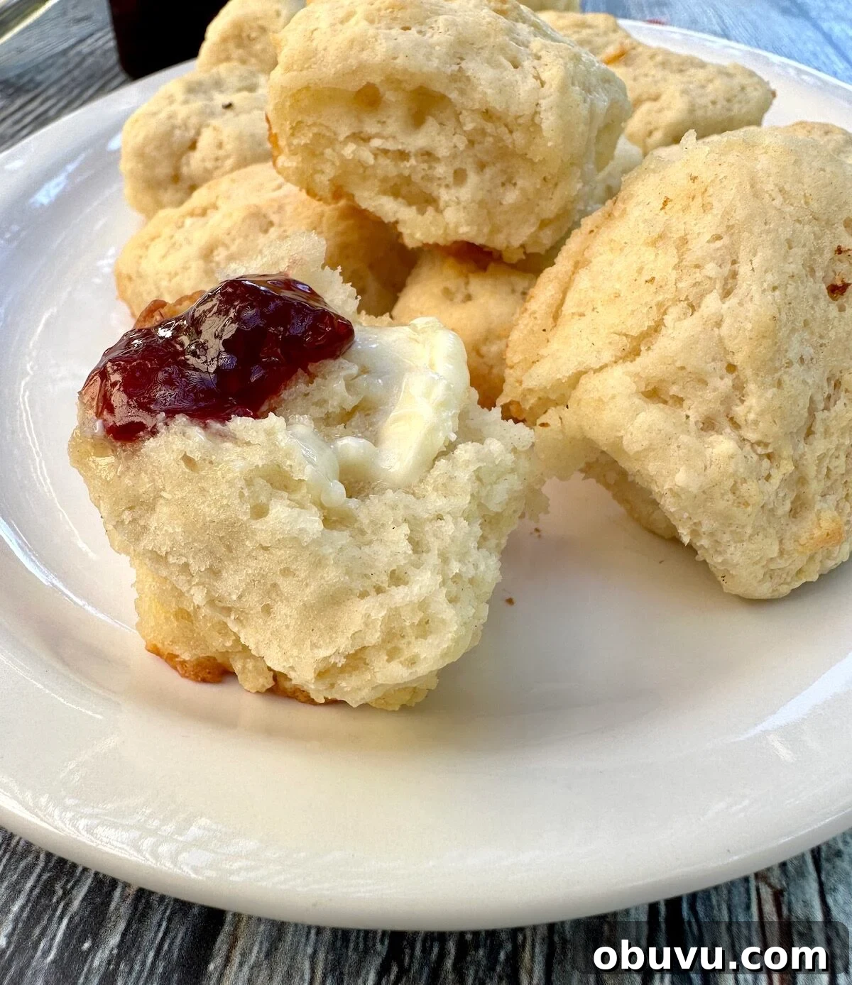 Flaky Buttermilk Biscuits Recipe for Perfect Homemade Biscuits 8 Biscuits on a plate, with one spread with jam and butter.