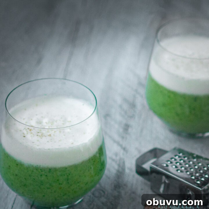 two glasses broccoli soup with a cream topping and some nutmeg