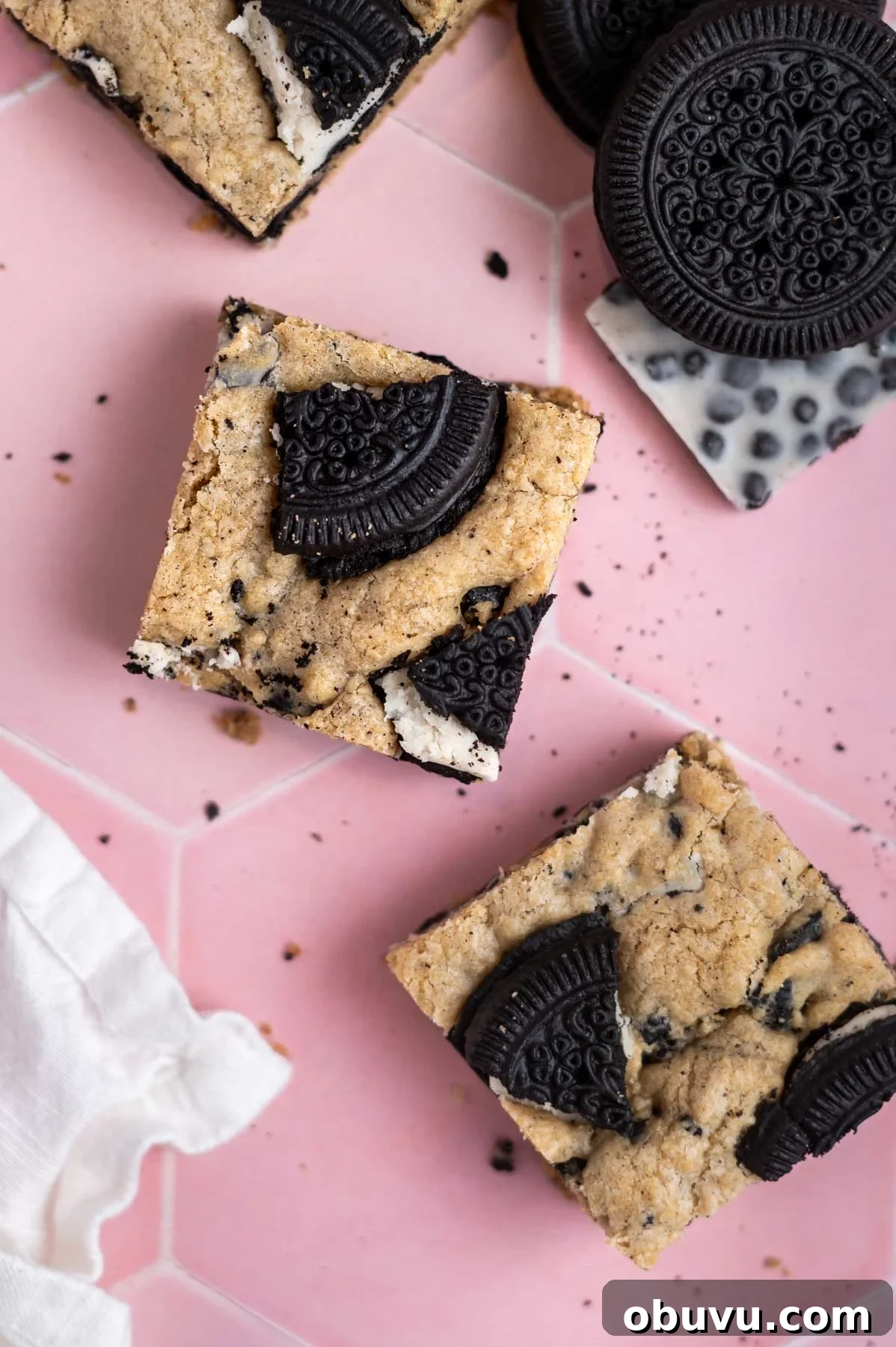 Soft Cookies and Cream Bars Recipe — Chewy & Irresistible 3 bar cookie squares on a counter with a napkin and extra cookies and candy bars