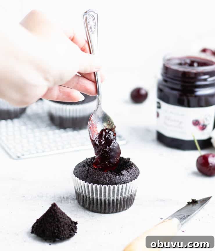 spooning cherry jam into the center of a chocolate cupcake.