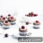 chocolate cherry cupcake on a plate in front of a cooling rack of cupcakes.