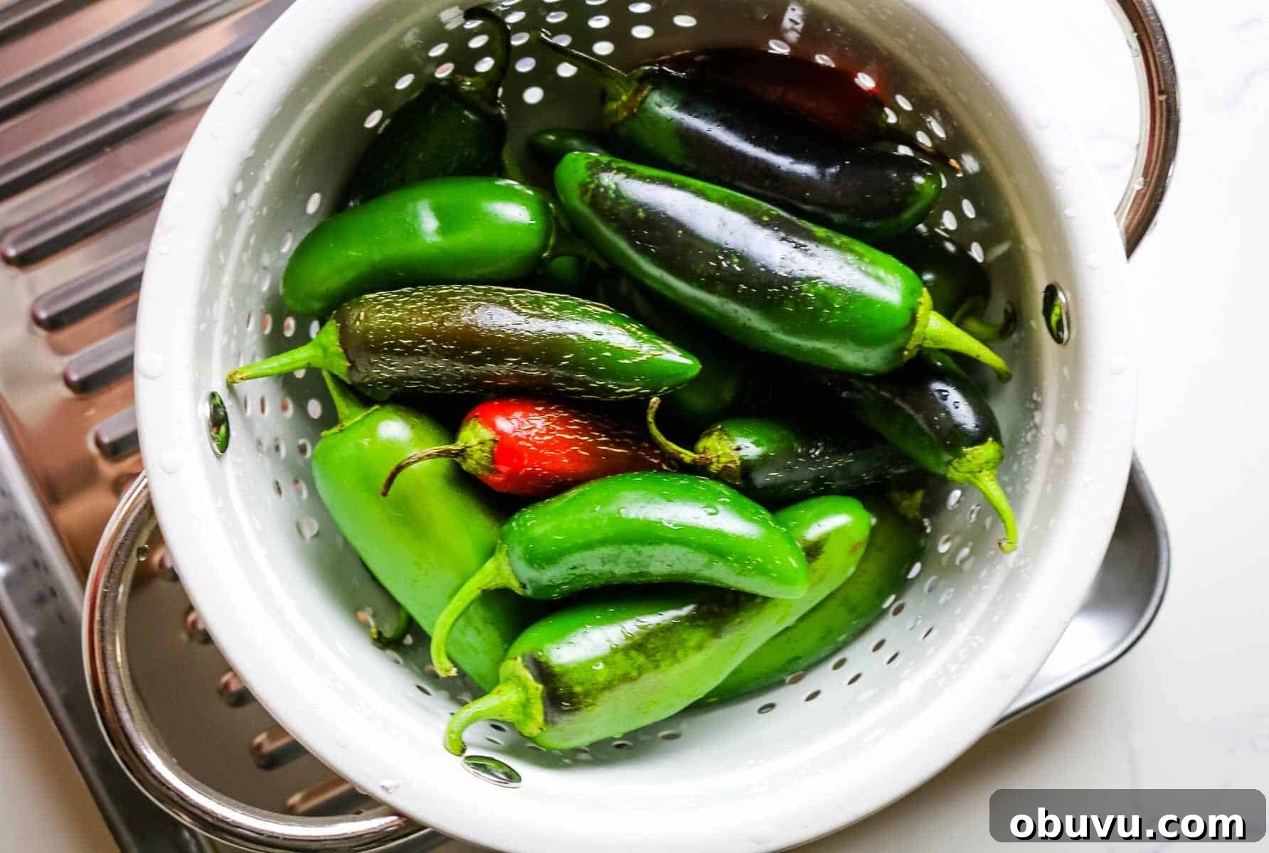 Charred Jalapeños: How to Roast and Use Smoky Peppers 4 jalapeno peppers in a colander on a sheet pan.