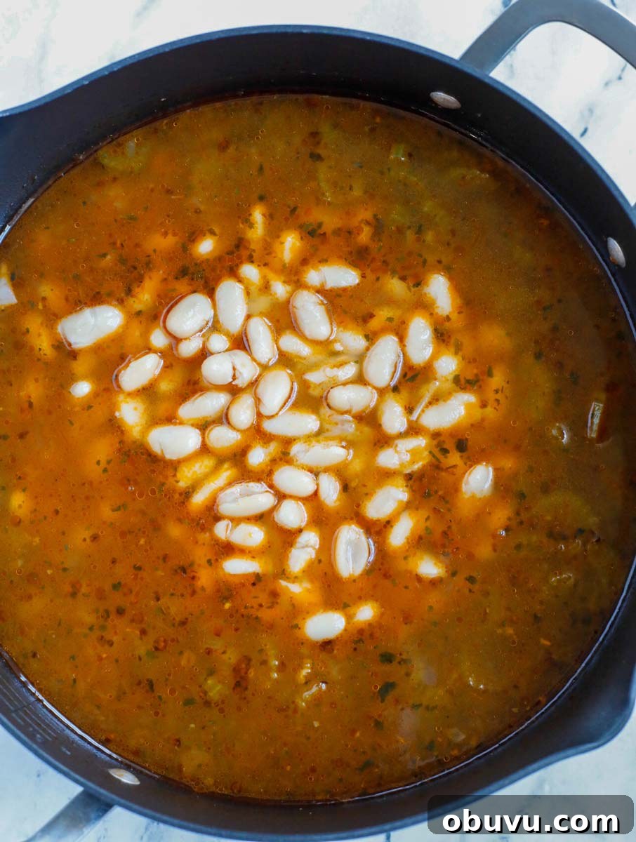 Authentic Tuscan White Bean Soup Recipe for Cozy Weeknights 6 White beans being added to a pot of soup.