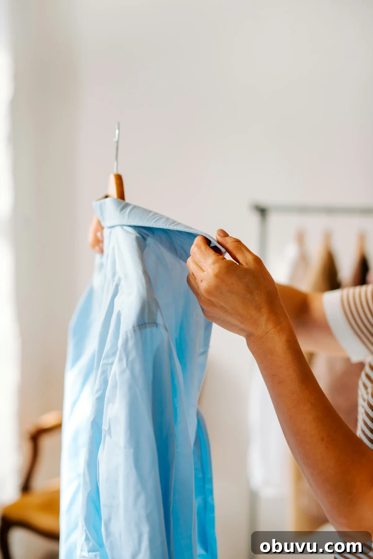 100 Satisfying Activities to Do Instead of Shopping 2 Close-up of a person examining a light blue button-down shirt on a wooden hanger, symbolizing intentional wardrobe choices and mindful shopping habits.