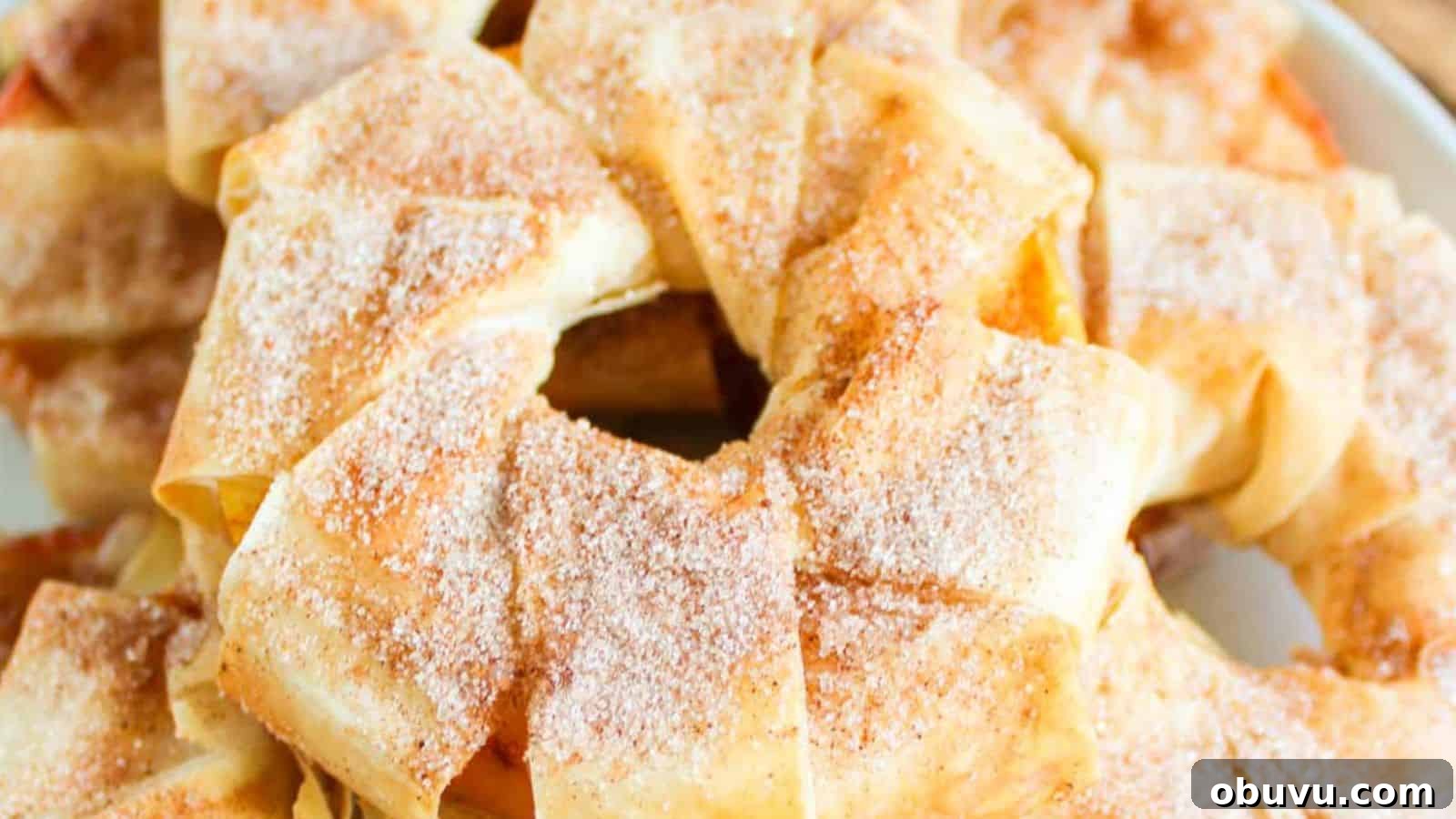 A close-up of a baked pastry ring dusted with powdered sugar, featuring multiple layers of golden-brown, flaky dough and hints of cinnamon apple strudel slices peeking through.