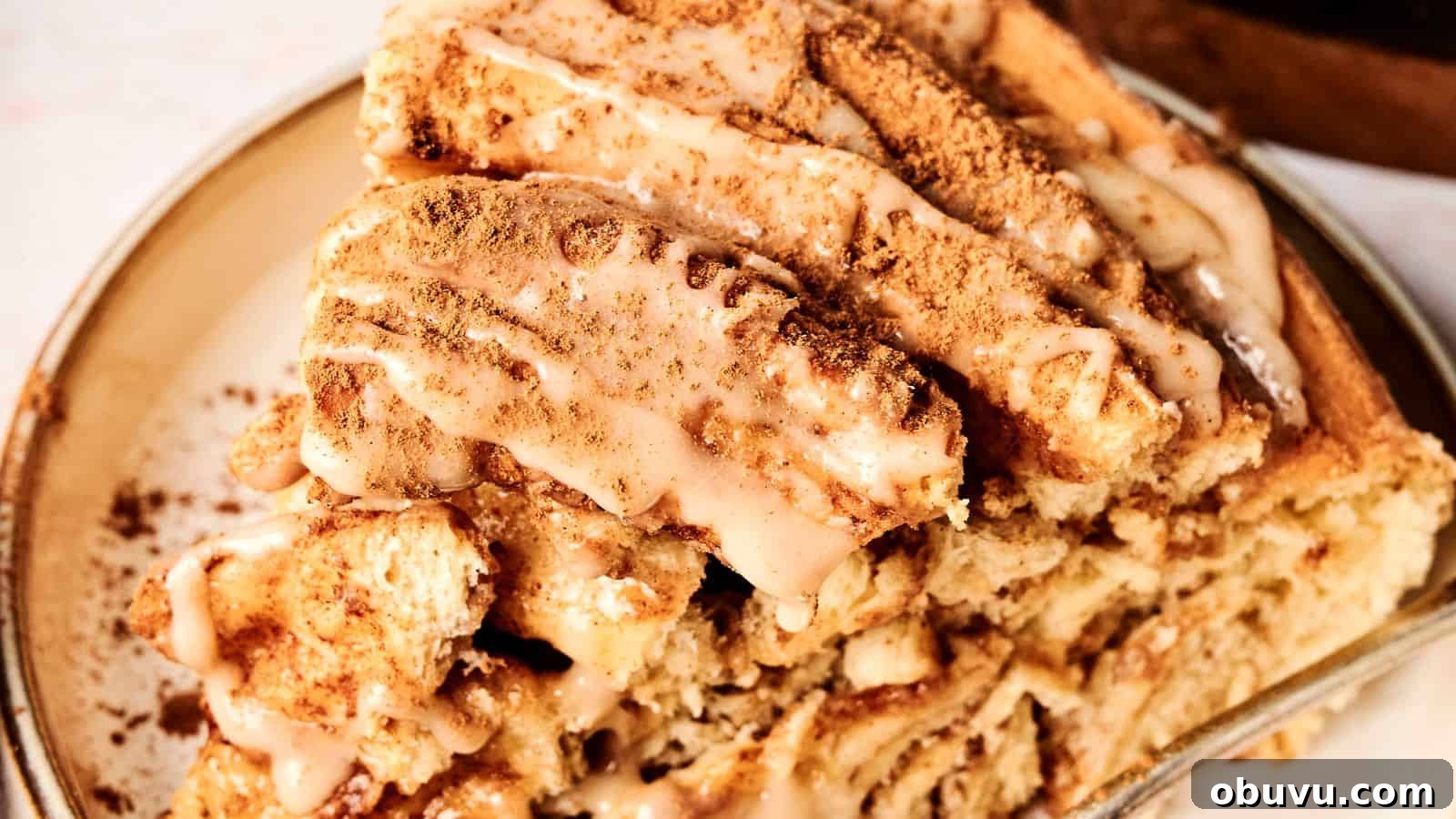 Close-up of a cinnamon roll cake slice topped with icing and sprinkled with cinnamon on a plate.