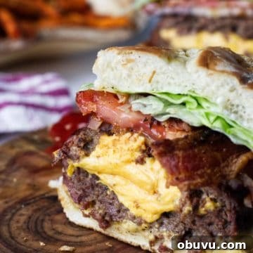Juicy Lucy Burger Recipe: Melted Cheese-Stuffed Patties 8 A Juicy Lucy bacon burger cross section, sitting on a wood cutting board, cheese spilling out the middle with bacon, onion, tomato, lettuce, with sweet potato fries in background