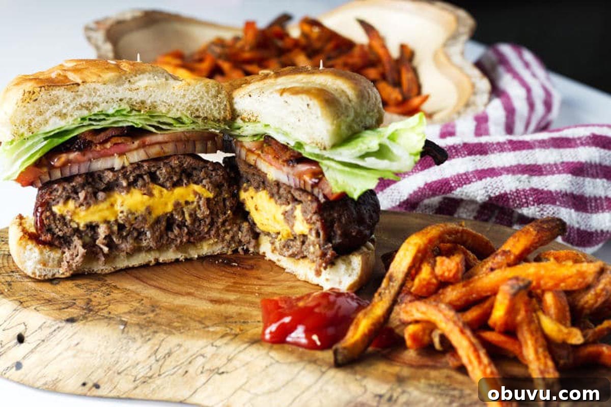 Juicy Lucy Burger Recipe: Melted Cheese-Stuffed Patties 6 A burger cut cross section, cheese spilling out the middle with bacon, onion, tomato, lettuce with sweet potato fries and ketchup.