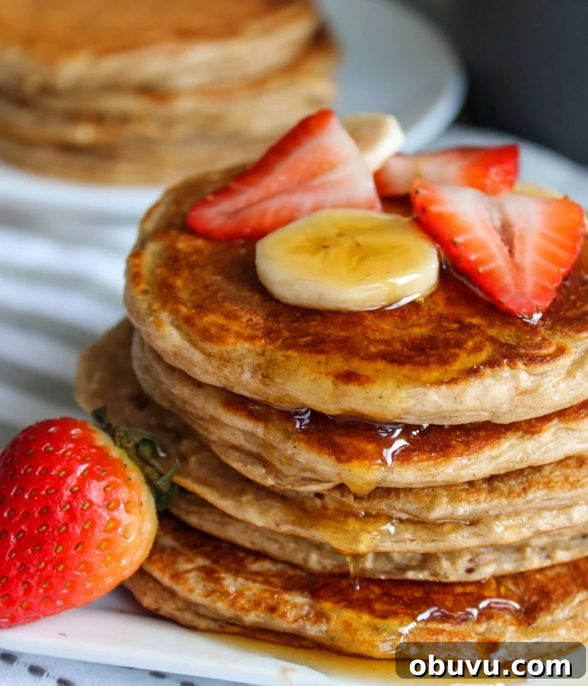 High-Protein Pancake Recipe for More Muscle and Energy 2 Stack of pancakes topped with strawberries and bananas with pure maple syrup poured on top.