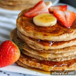 High-Protein Pancake Recipe for More Muscle and Energy 9 a stack of pancakes on a plate topped with strawberries and bananas with pure maple syrup