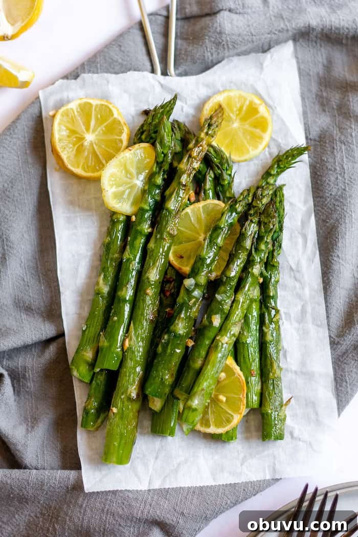 Image shows a parchment paper with stalks of asparagus and lemon rounds on it, resting on a grey towel
