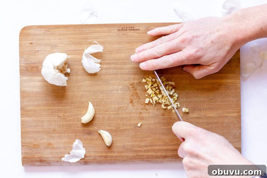 Image, taken from above, shows a hand dicing garlic into small pieces