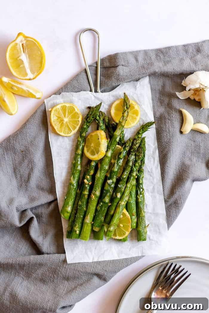Image, taken from above shows the garlic and lemon asparagus vegetable side dish on a grey towel. Several stalks of asparagus are coated in garlic and lemons.