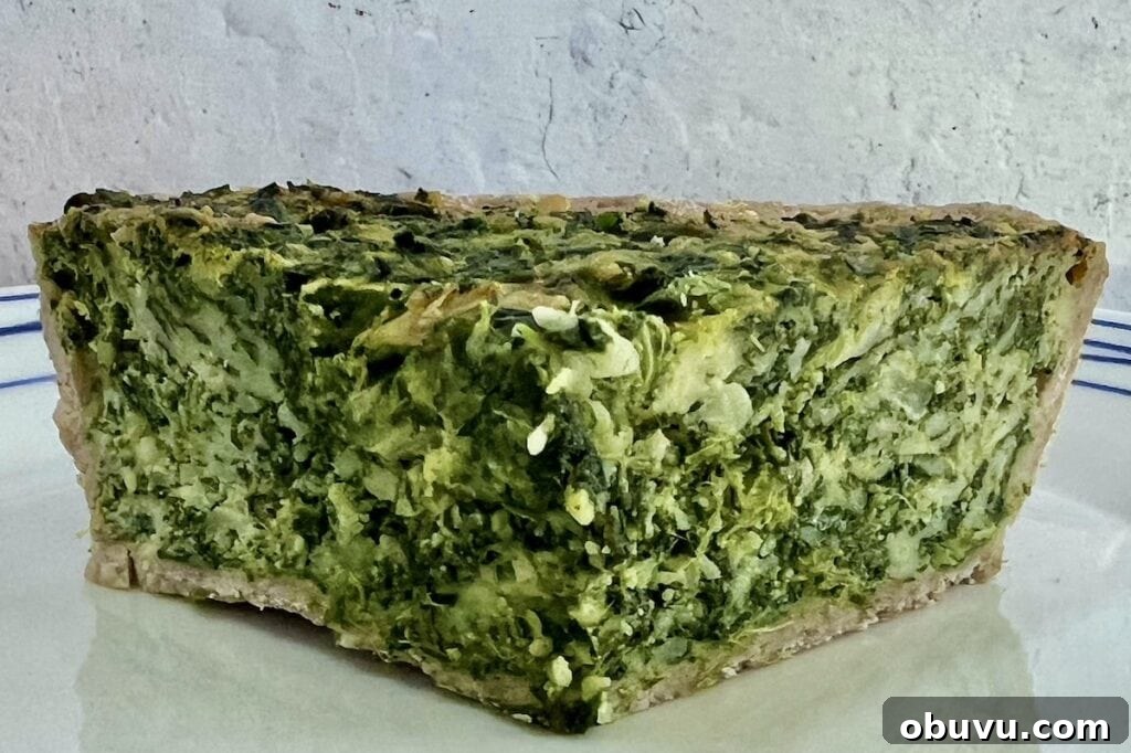 Spinach and Swiss Quiche with Frozen Pie Crust 5 Front view of a slice of spinach swiss quiche on white plate, demonstrating its thickness and density.