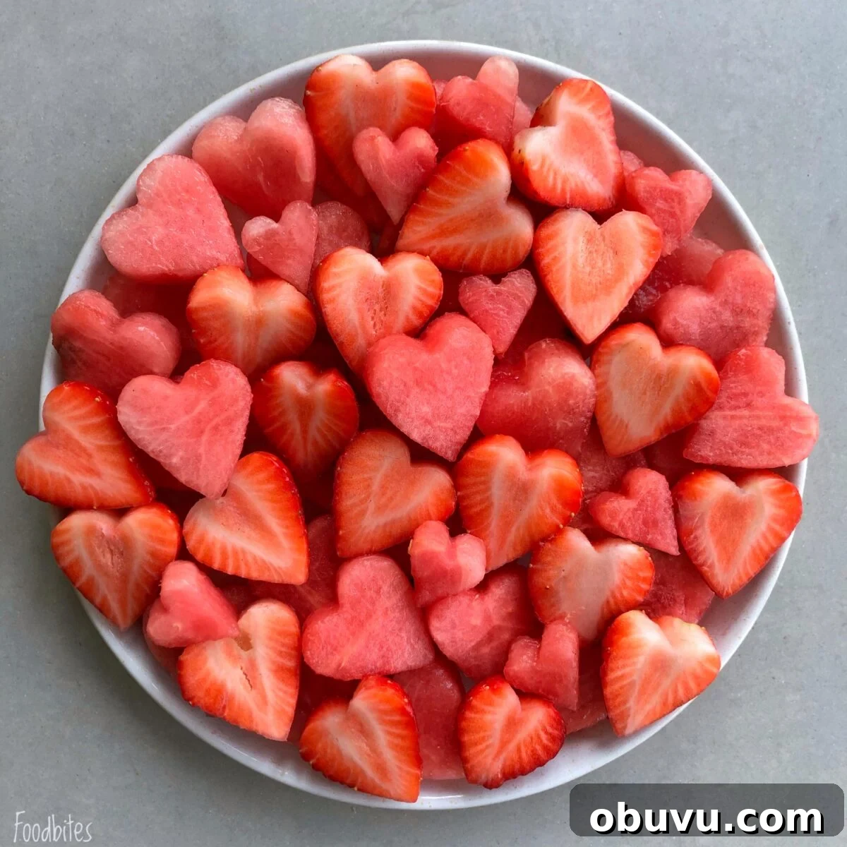 Refreshing Watermelon Fruit Salad with Mint and Lime 2 A white plate filled with heart-shaped pieces of watermelon and strawberries on a light gray surface.