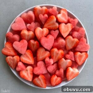 Refreshing Watermelon Fruit Salad with Mint and Lime 4 A white plate filled with heart-shaped pieces of watermelon and strawberries on a light gray surface.