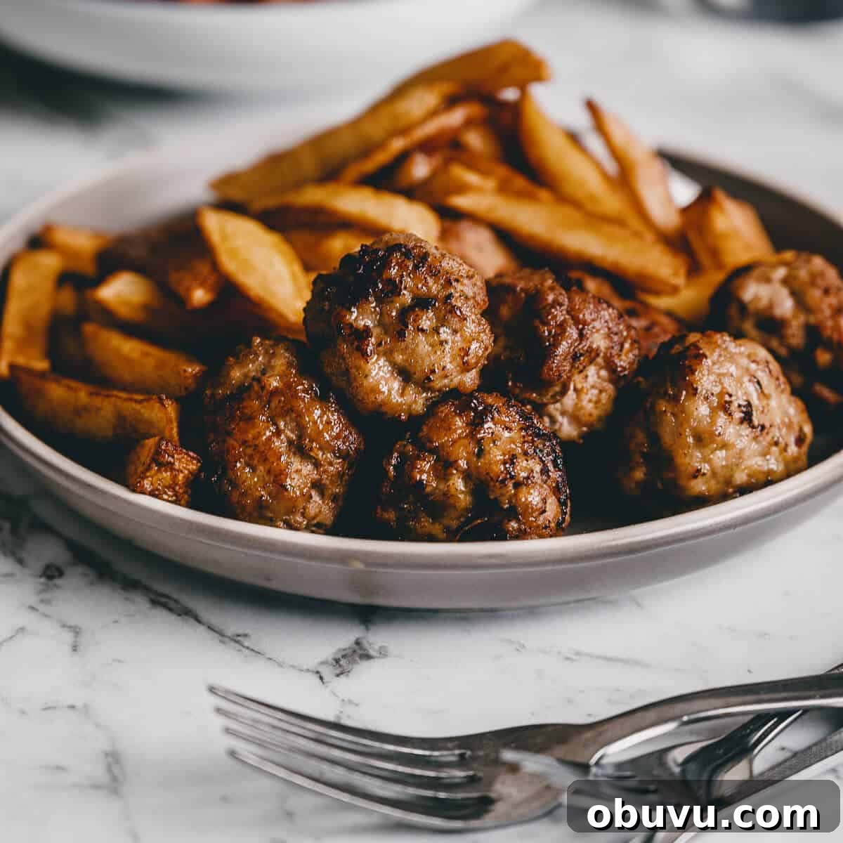 close up of fried meatballs with french fries in the background.