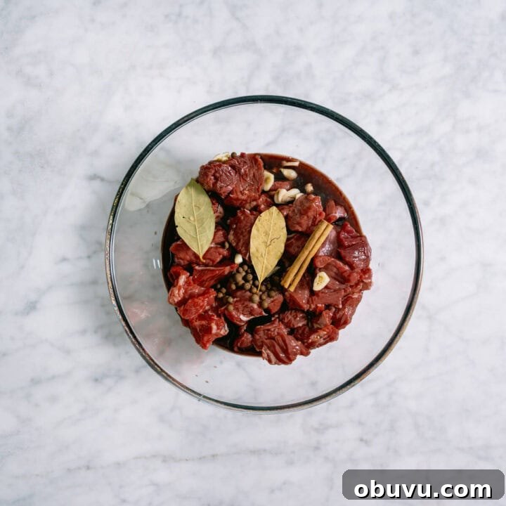 chuck steak and spices marinating in a glass bowl.