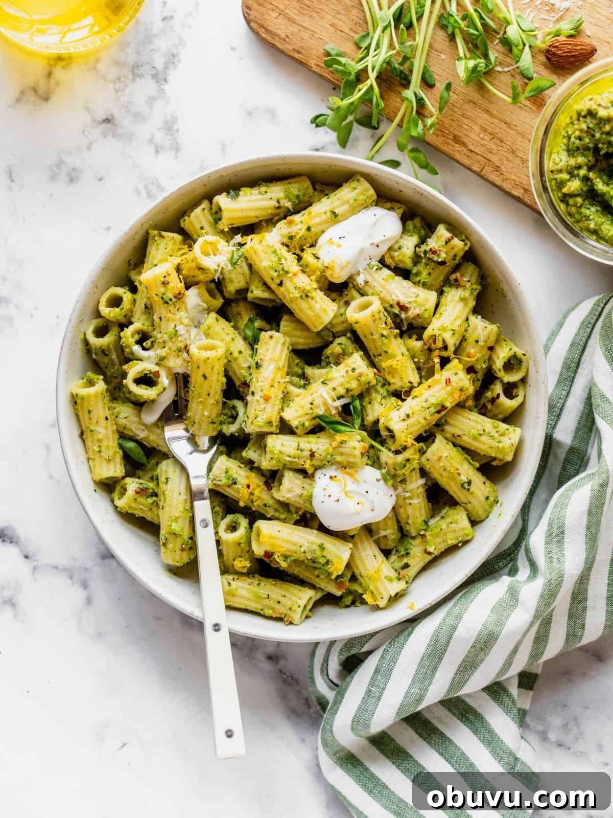 Bowl of pasta tossed with pea pesto and garnished with pea shoots, dollops of cream and cheese.