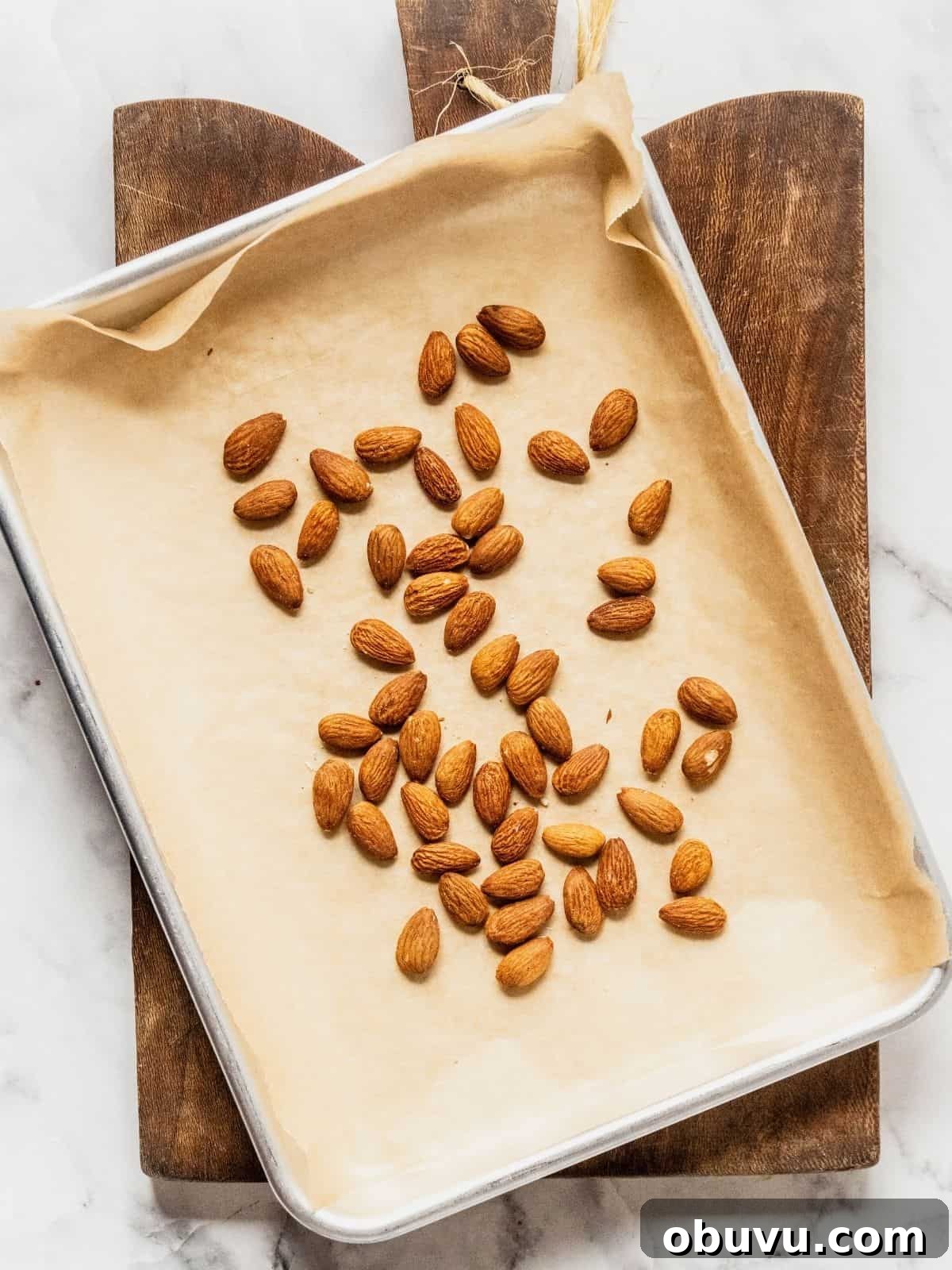 Parchment paper lined baking tray with almonds on it.
