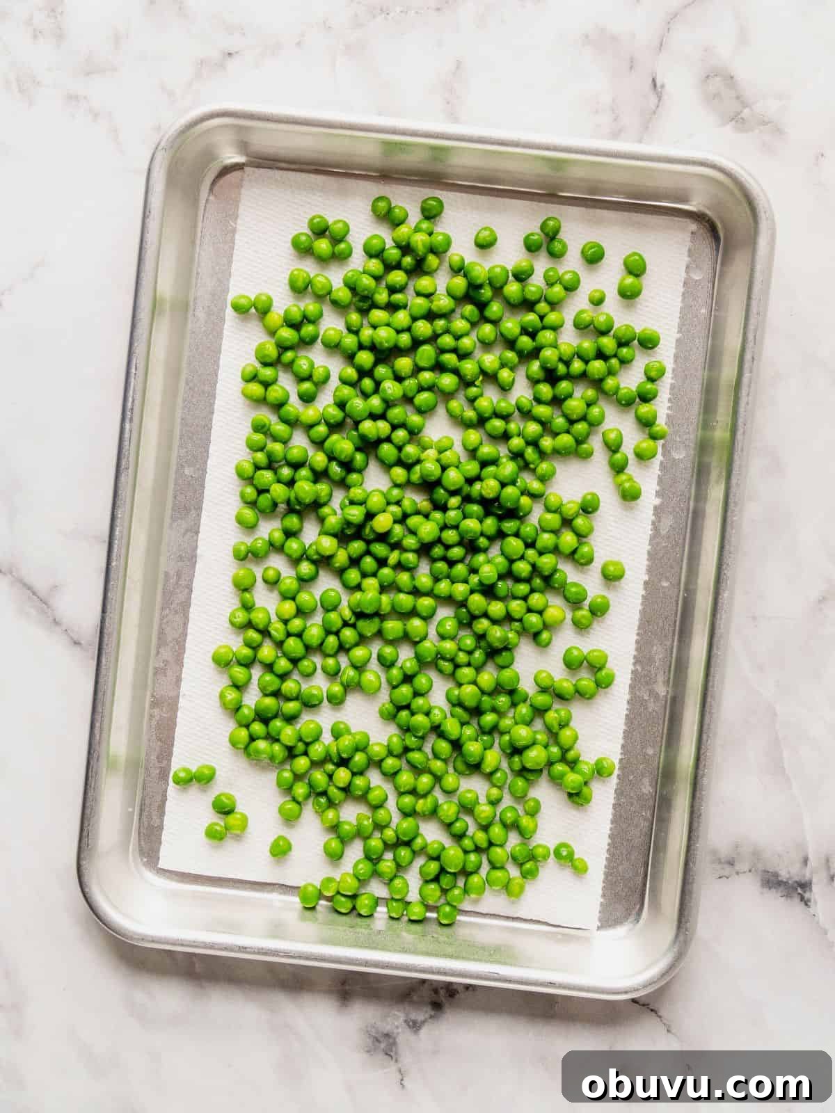 Paper-lined baking sheet with peas draining.