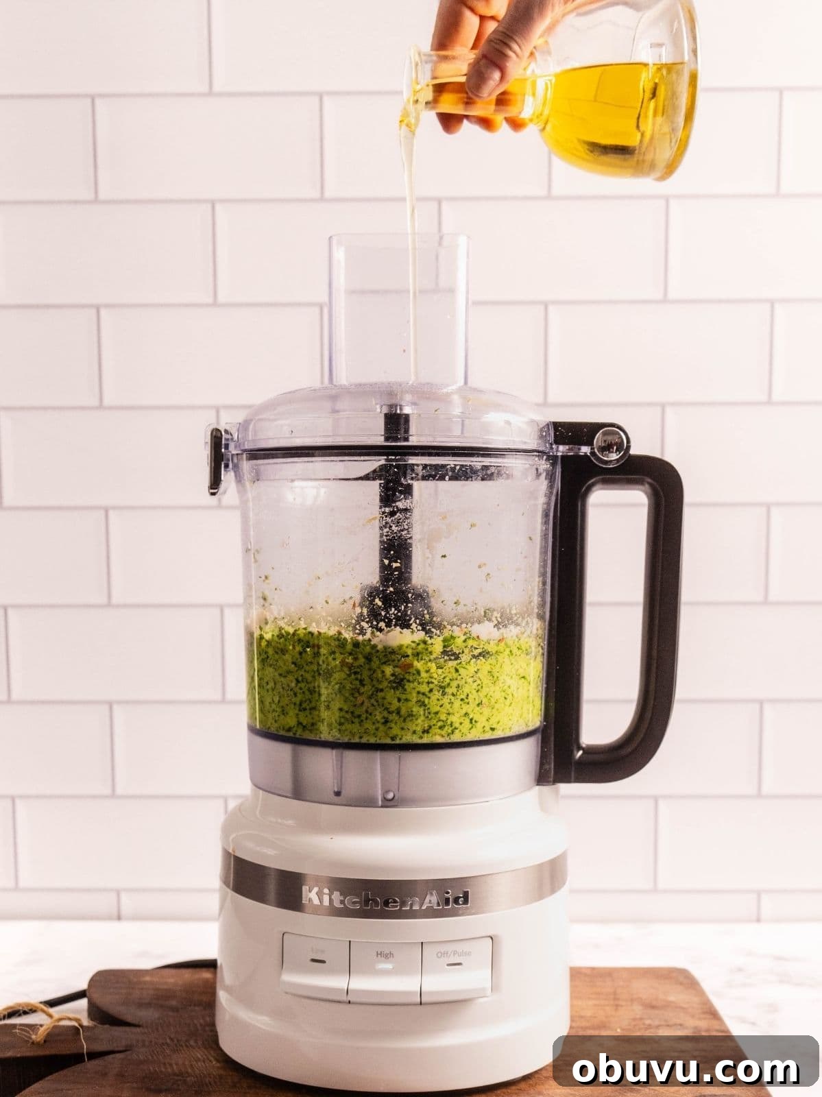 Drizzling olive oil into the food processor as it processes the pesto.