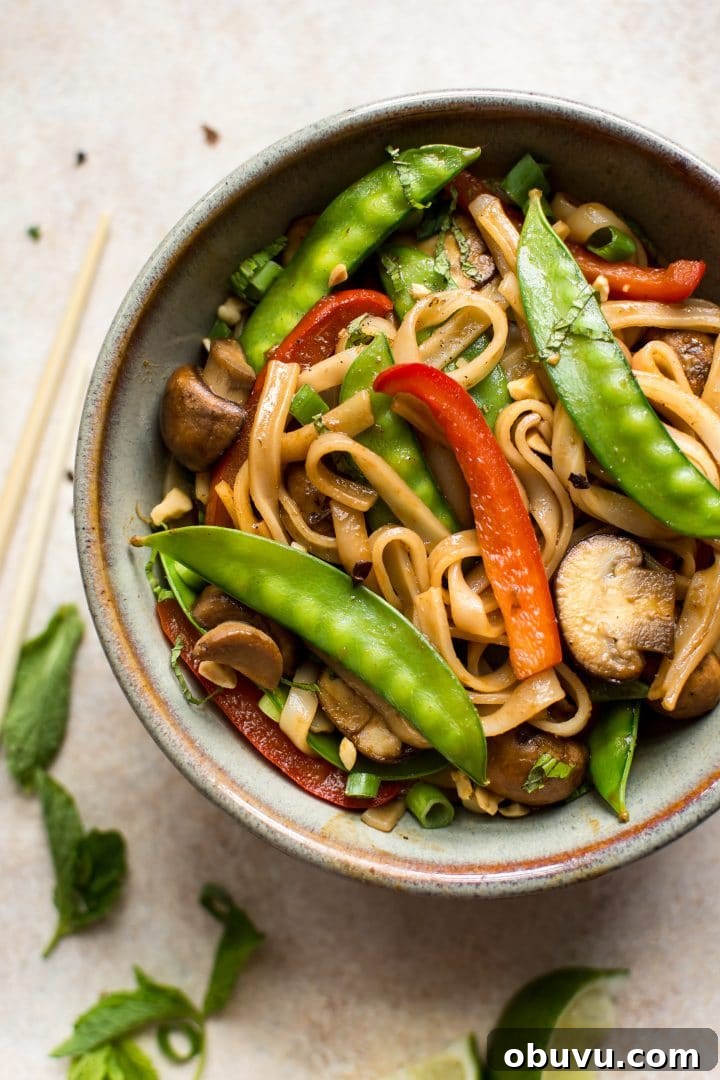 Flavorful Vegan Rice Noodle Recipes for Every Meal 2 close-up of vegan rice noodle stir fry with peas, mushrooms, and red peppers in a bowl beside chopsticks
