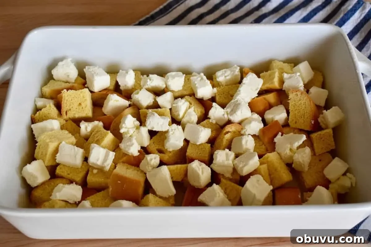 Cream Cheese Baked French Toast Casserole Recipe 5 Cubed bread in a white baking dish with chunks of cream cheese sprinkled on top.