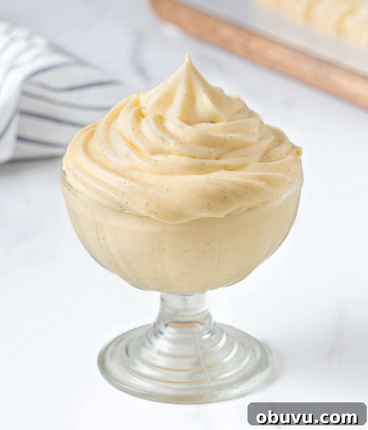 Cream piped into a small glass cup with a tea towel and serving board in the background.
