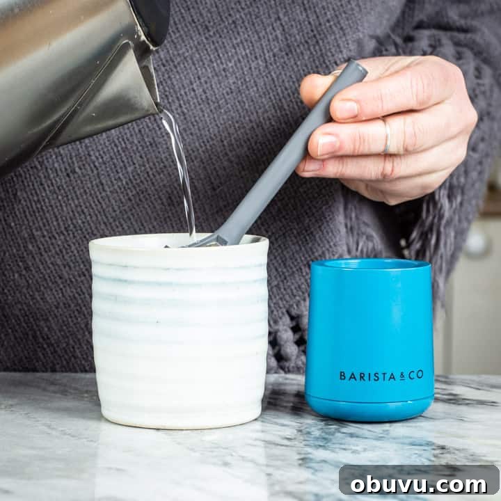 Brew It Stick Review — Is This the Ultimate Camping Coffee Maker? 9 womans hands pouring water from a kettle into the brew it stick coffee maker into a handmade mug on a marble surface