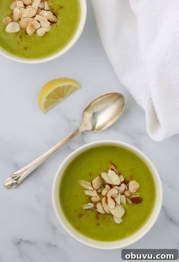 A bowl of zucchini soup topped with almonds and a spoon and lemon wedge